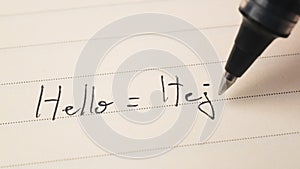 Beginner Swedish language learner writing Hello word Hej for homework on a notebook photo