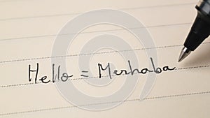 Beginner Turkish language learner writing Hello word Merhaba for homework on a notebook