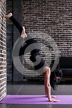 Beginning female yogi practicing yoga inversion poses standing on hands upside down leaning against wall in fitness club