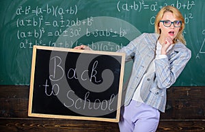 Beginning of new school season. Woman teacher holds blackboard inscription back to school. Lady educator in classroom