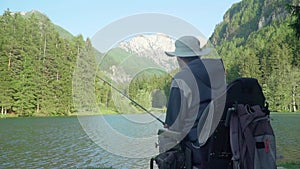 Behind the back slow motion of handicapped fisherman in a electric wheelchair fishing in beautiful lake near forest and