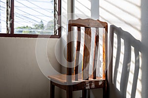 Behind the back of a wooden chair with the sunlight louvered windows onto the wall of the room