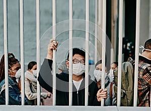 Behind bars, lockdown and covid restrictions with a man wearing a mask during a pandemic and travel ban. Portrait of a