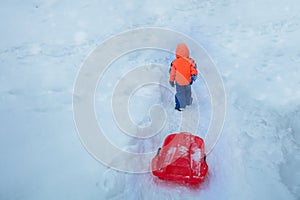 From behind boy pull on uphill with sled, at winter vacations