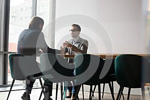 Behind glass wall two businessmen negotiating seated at boardroom desk