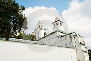 Behind a high white stone wall there is a large old Orthodox church with two belfries, a wooden and green roof and golden domes an