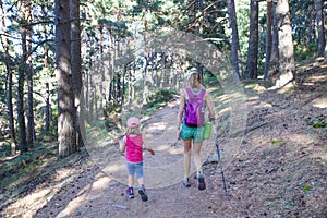 From behind mountaineers woman and little girl hiking on trail in forest near of Madrid