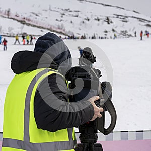 Behind the scene. Sports cameraman with video camera, back to us, shooting sports scenes on a ski slope