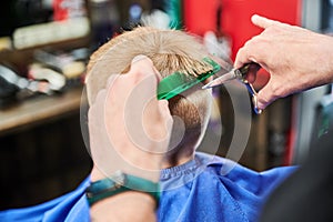 Behind shoulder view of male barber cutting little boy& x27;s hair.