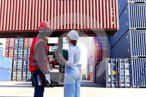 Behind two workers wear safety vest and helmet discussing at logistic shipping cargo container yard. African American engineer man
