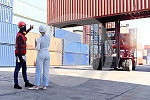 Behind two workers wear safety vest and helmet discussing at logistic shipping cargo container yard. African American engineer man