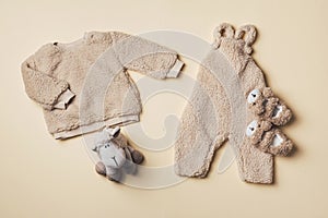 Beige baby teddy bodysuit, sweatshirt, soft toy sheep on pastel backgroundd. Styled newborn clothes. Copy space. Flat