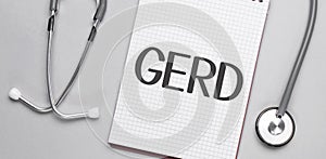 On a beige background, a stethoscope and a white notepad with the inscription GERD .Medical concept