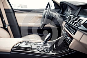 Beige and black interior of modern car, close-up details of automatic transmission and gear stick against steering wheel ba