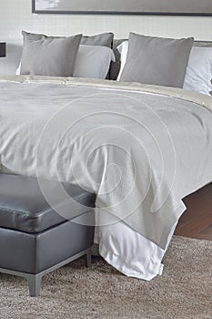 Beige blanket on comfy bed with black leather ottoman in bedroom