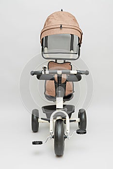 Beige children`s tricycle with a handle on a gray background, front view