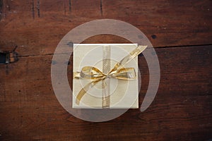 Beige closed gift box with gold color ribbon on wooden table background