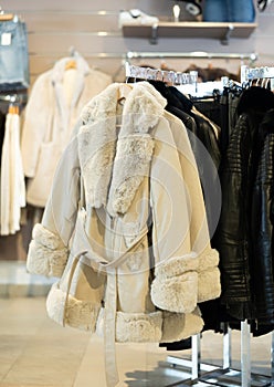 Beige coat with fur collar and sleeves hanging on stand in clothing store