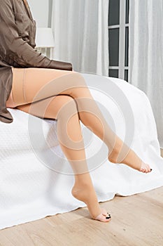 Beige compression stockings on a woman in a white room. Girl putting on stockings at home. Beautiful female legs