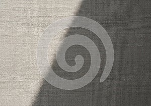 A beige fabric surface with a diagonal shadow. The textile's texture is