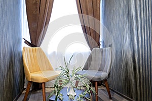 Beige and gray chairs near a wooden table with a vase and a houseplant on it,against a window with white tulle and coffee curtains