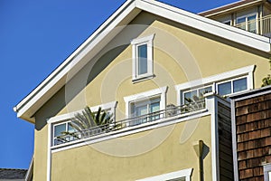 Beige house facade with white accent paint around inwos and near roof with balcony and potted plants on porch