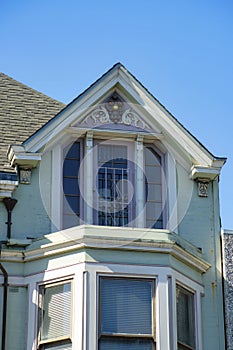 Beige house facade with white accent paint near roof and brown tiles with double gable design and blue sky background