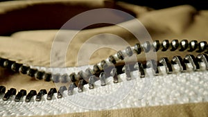 Beige jacket with an unbuttoned metal zipper in macro. Extreme close up of the zipping and fabric structure of the
