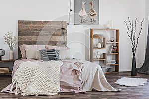 Beige, knit blanket on a pink bed with wooden bedhead in rustic bedroom interior for a woman
