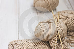 Beige Merino yarn with bamboo needles on white wooden background
