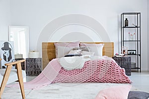 Beige pillows and fury white blanket on big comfortable bed in bright bedroom interior, copy space on empty white wall