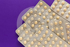 Beige pills inside medicine box. Purple background.