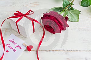 Beige polka dot gift box with red ribbon bow and bautiful red roses on wooden background. Greeting card for holiday
