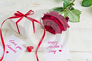 Beige polka dot gift box with red ribbon bow and bautiful red roses on wooden background. Greeting card for Mother`s day