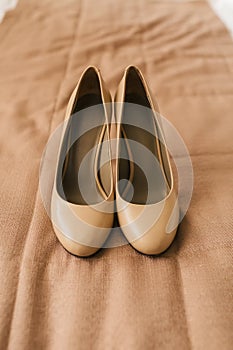 Beige shoes on heels of a bride on a brown textile background. Wedding preparation. Artwork.