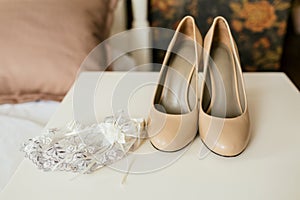 Beige shoes on a heels and lace garter on a white table. Wedding preparation. Artwork