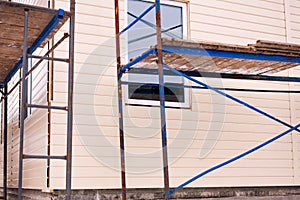 Beige siding covering the wall and scaffolding around the house