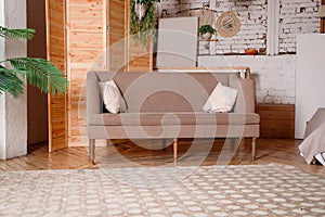 Beige sofa on a brick wall background. Nearby is a houseplant with large leaves and a screen made of natural wood