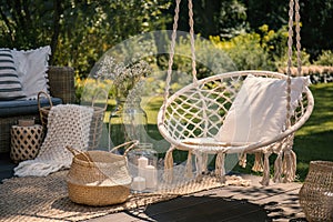 A beige string swing with a pillow on a patio. Wicker baskets, a