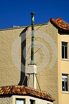 Beige stucco exterior on house or home with metal chimney vent and adobe style red roof tops with blue sky background