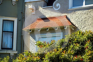 Beige stucco home exterior with adobe red small roof tiles and green house next door with front yard trees and hidden