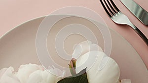 Beige table setting with peony flowers on plate and silverware for luxury dinner party, wedding or birthday celebration