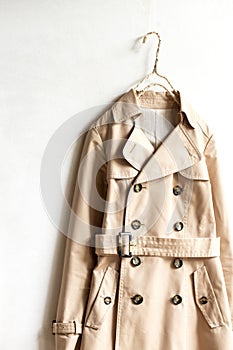 Beige trench coat isolated hanging on a hanger in a white wall