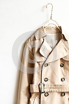 Beige trench coat isolated hanging on a hanger in a white wall
