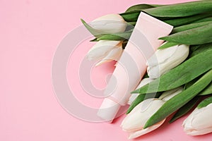 Beige tube with cosmetic cream or lotion for body and bouquet of white tulips, pink background, copy space