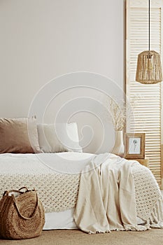 Beige and white pillows on comfortable bed, flower in vase and picture in frame on nightstand, copy space on empty wall