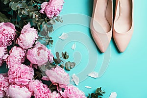 Beige women shoes nude shoes, pink peonies, eucalyptus flower on blue background. Flat lay, top view. Copy space. Floral mock up.