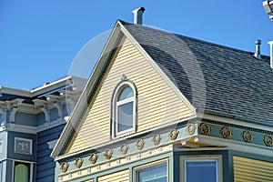 Beige wood slattted pannels on home with green accent beams near roof with tiny window and brown tiles and neighboring