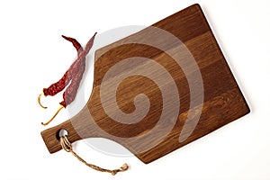 A beige wooden cutting board and two dried hot pepper pods isolated on a white background