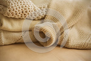 Beige wool warm sweaters lie on the bed, folded in a pile. Warm clothing for cold autumn and winter